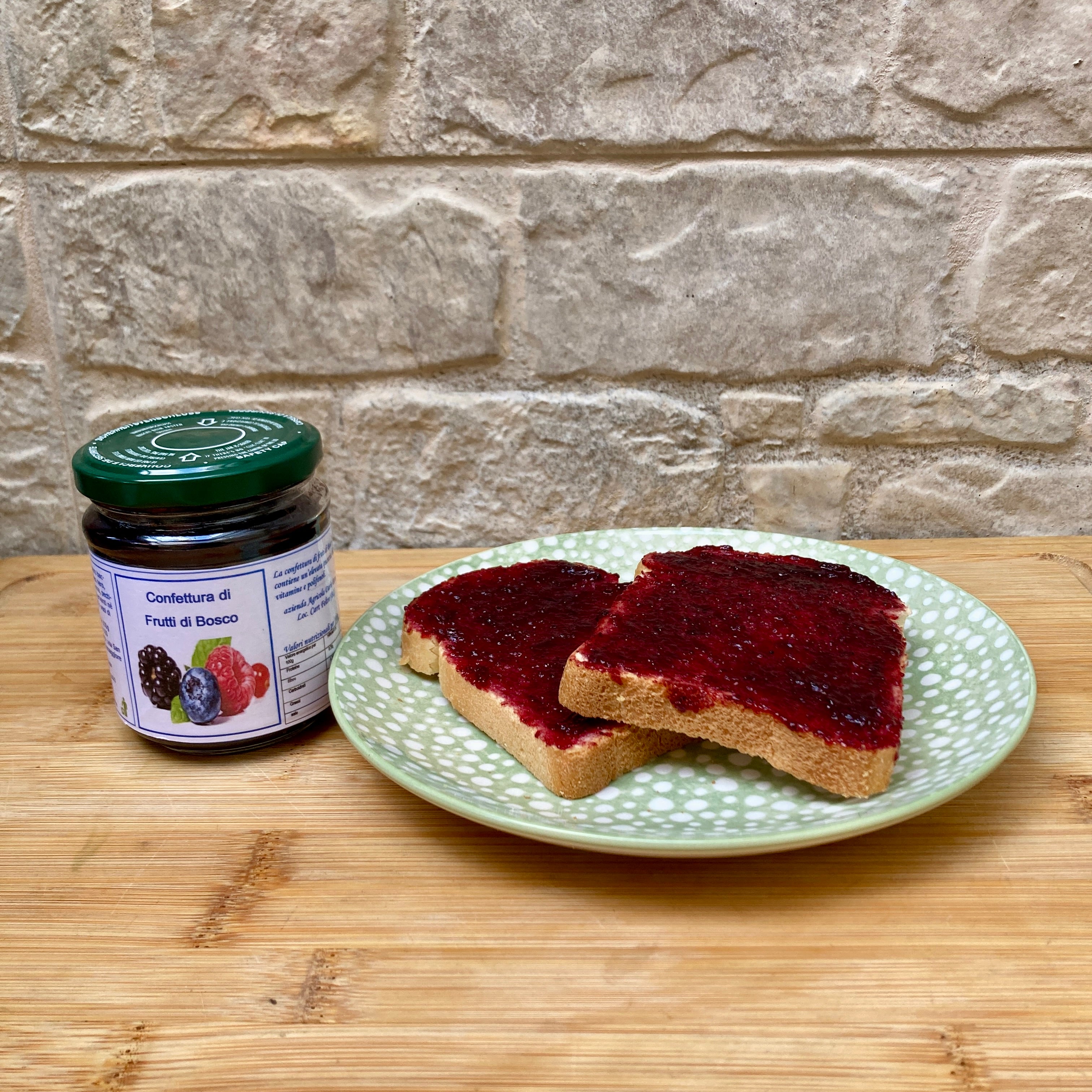 foto che contiene un barattolo di confettura ai frutti di bosco, di fianco è presente u piatto contenente due fette di pane con la marmellata